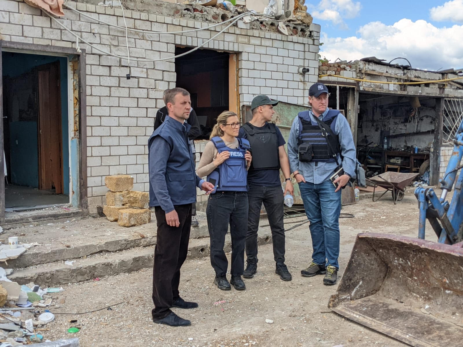 Erin McLaughlin in a press vest reporting with her crew outside a shelled and damaged building
